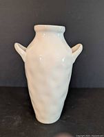 Front view of white ceramic vase with two small handles on a dark background.