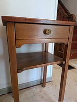Front angled view of wood table showing drawer with decorative knob and lower shelf.