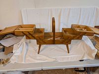 Wooden sewing box fully opened showing multiple articulated compartments and small trays for organizing sewing supplies.