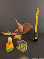 Wooden swordfish sculpture with measuring tape for scale and two cat figurines in foreground