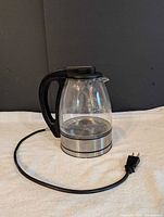 Electric glass kettle with black handle, stainless steel base, power cord and plug