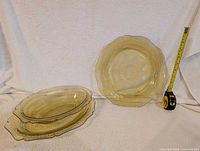 Four yellow depression glass plates displayed, three oval and one round, with a tape measure for size reference (approx. 10 inches).