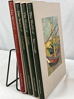 Four hardcover art books standing upright on a metal display stand, clearly showing their paperboard slipcases and spines.