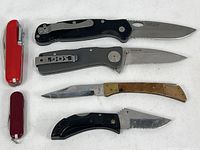 6 folding knives laid out, showing handles and blades closed and open, varied styles and colors.