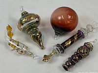 Top-down view of all five hand blown glass ornaments arranged on a white background, showing their size, shapes, and gold glazing details.