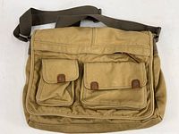 Front view of tan canvas Fossil Cruiser shoulder bag with two flap pockets secured by snap buttons and adjustable shoulder strap