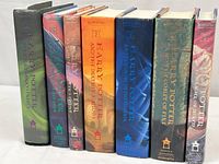 Seven hardcover Harry Potter books standing upright showing spines with titles and author J.K. Rowling. Dust jackets intact.
