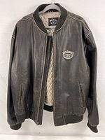 Front view of the dark brown leather jacket with the Jack Daniel’s label inside and logo embroidered on front chest, zipper partially open revealing quilted lining.