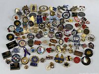 Various enamel pins laid out on a white surface showing police badges, motorcycle helmets, flags, and symbolic icons.