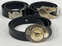 Three black leather belts rolled next to their respective buckles: buffalo nickel themed oval buckle with bison head, silver eagle buckle, and a braided leather belt.