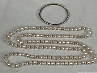 Pearl necklace laid out in three rows with silver-tone decorative bangle bracelet placed above it, showing overall size and appearance.
