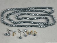 Full view of 50-inch gray pearl necklace alongside three pairs of clip-on pearl earrings showing overall lot contents