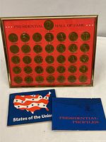 Framed collection of 37 presidential bronze medallions on red background with two blue booklets in front.