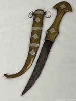 Full view of the dagger and matching sheath showing brass and silver-tone decorations with curved blade and sheath tip.