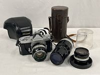 Nikomat camera with attached 50mm lens, 200mm lens in leather case, 28mm lens in plastic case, and black leather carrying pouch.