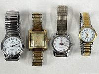 Photo showing all four watches side by side: Iwei Quartz X028, two Timex watches, and one unknown brand, all with expandable metal bands.