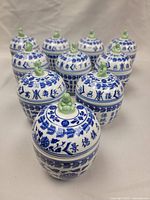 Front angled view of all 10 blue and white Chinese porcelain spice jars arranged together, showcasing their blue calligraphy and green Buddha figurines on lids.