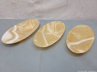 Three oval polished onyx marble coin dishes with yellow and white natural veining placed side by side on a surface.