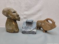 Three stone sculptures: human head bust, abstract geometric form, buffalo-like animal figure.