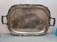 Full view of large rectangular silver plate serving tray with decorative handles and ornate rim.