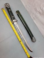 Traditional Japanese short sword and green wooden sheath placed side by side with a measuring tape showing approximately 42 cm blade length; sheath wood has visible damage near top.