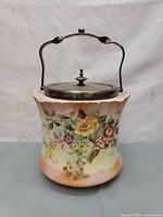 Full view of antique biscuit barrel showing floral peony decoration, scalloped rim and metal handle and lid