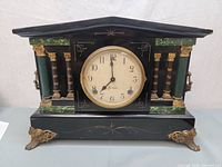 Front view of the antique Sessions Wabash mantle clock showing black case with green and gold decorative columns and feet, clock face centered