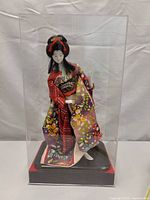 Front view of Asian woman doll in a colorful kimono inside a transparent acrylic display case showing her full figure and detailed clothing.