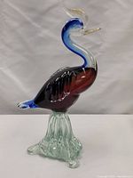 Front and side view of the colorful glass bird sculpture with clear glass base on white background.
