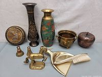 Full view of all metal items including vases, unicorn figurine, bells, dustpan and brush, brass pot, and apple-shaped container