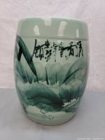 Front view of cylindrical ceramic stool showing light green glaze with dark green leaves and black calligraphy painted on the side.