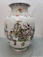 Front view of the vase showing hand-painted figures and colorful floral designs on glossy white porcelain.