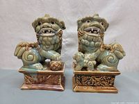 Front view of two ceramic Chinese guardian lions on rectangular bases, showing facial details and positioning of paws.