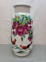 Front view of porcelain vase showing lychee fruit cluster with two roosters beneath on white background.