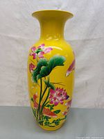 Front view showing bright yellow ceramic vase decorated with pink lotus flowers, green leaves, and colorful fish.