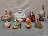 Overview photo showing all eight figurines including Budai Laughing Buddha figures, seated characters, pig with baby, and rooster.