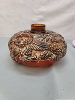 Side view of the round amber glass vase showing raised floral and apple pattern with gold and brown highlights