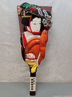 Full front view of hagoita paddle with detailed geisha fabric art and painted floral patterns.