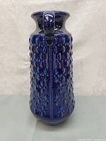Front view of tall blue ceramic vase with textured raised rounded dots and single handle near the mouth.