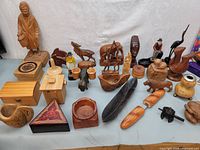 Photo showing a large group of hand crafted items including wooden figurines, carved animals, container boxes, and decorative knives all arranged on a flat surface.