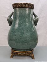 Front view of the green celadon crackle glazed porcelain vase with double ears, sitting on ornate metal stand, showing overall shape and glaze surface with crackle pattern