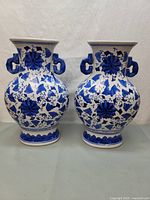 Front view of the pair of blue and white ceramic vases showing floral and butterfly designs and decorative handles.