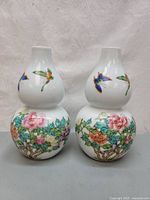 Front view of two double-gourd shaped white porcelain vases decorated with multicolor floral and fruit patterns on the bottom bulb and butterflies on the top bulb.