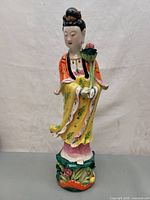 Front view of hand-painted Guanyin statue in colorful robes holding lotus flower.