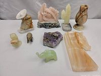 Full view of all stone sculptures showing various carved figurines, vases, and mineral cluster on a plain background.