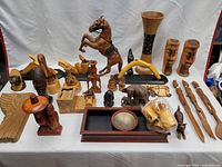 Photo showing full table display of assorted wood figurines and carved items including large horse, animals, and utensils.