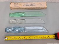 Three glass cutting utensils with green, clear, and blue decorative handles laid out with measuring tape and original box showing brand 'Vitrex-Gla'