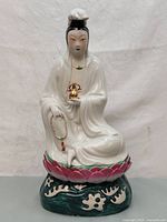 Front view of the vintage Chinese Quan Yin porcelain statue seated on a lotus base holding a golden bottle and rosary