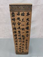 Photo of one side of the tall rectangular ceramic vase showing the black calligraphy poem and geometric border design on beige body.