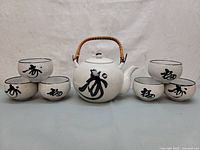 Front view photo showing the teapot centered with its handle up, flanked by three cups on each side, displaying the black calligraphy on cups.
